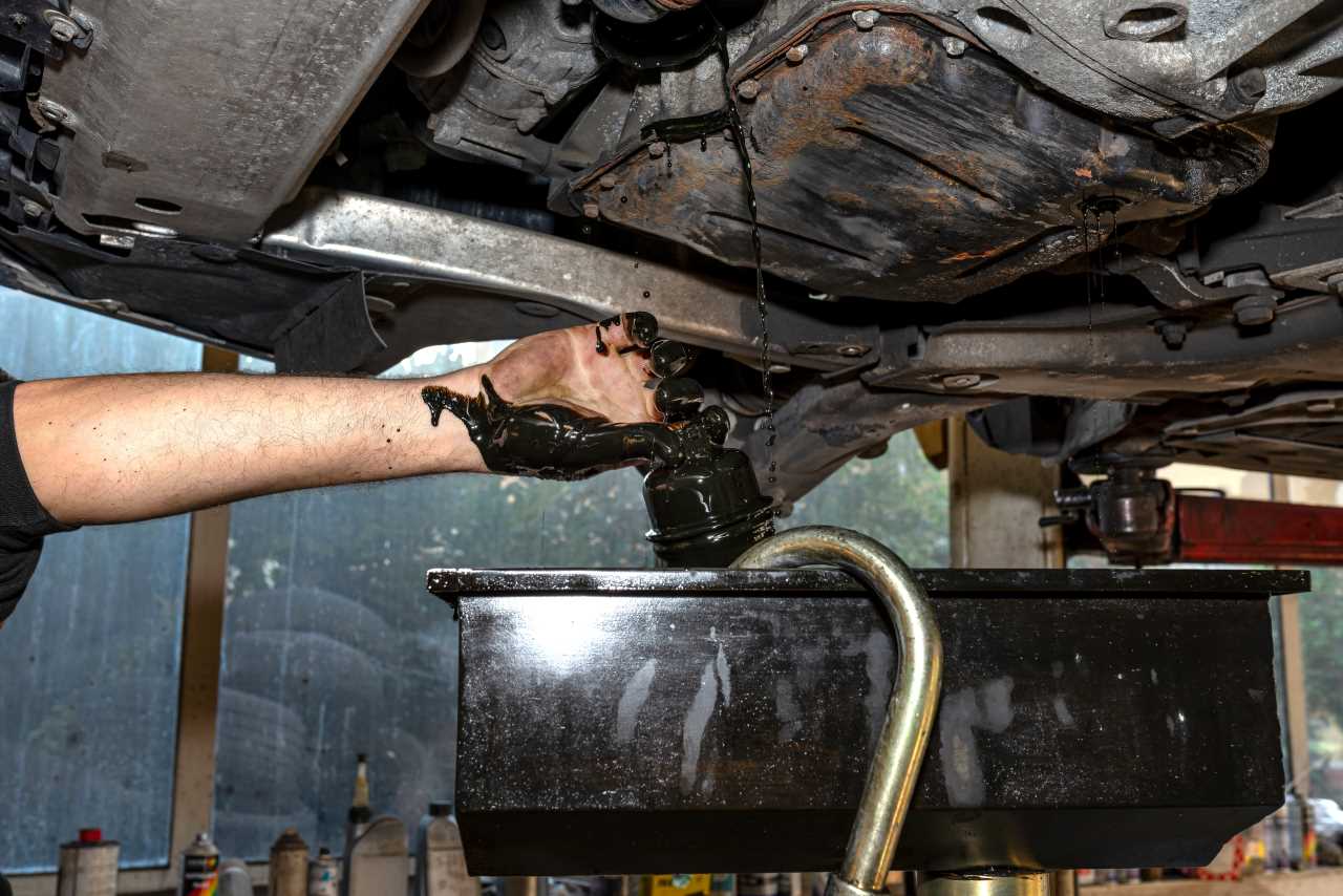 car engine oil leak, car mechanic draining oil from the engine